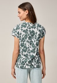 Zelené a bílé tričko s krátkým rukávem s leopardím vzorem, vyrobené z lehkého materiálu. Rovný lem a ohrnuté rukávy.