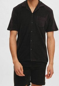 Camicetta nera a maniche corte con chiusura a bottoni, realizzata in morbido tessuto terry, con taschino sul petto e un design del colletto rilassato.