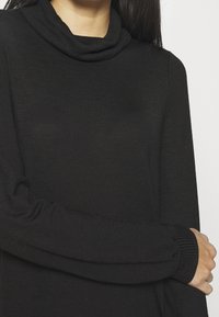 Schwarzer Rollkragenpullover mit lockerem Kragen, langen Ärmeln und gerippten Bündchen. Glatte Textur und figurbetontes Design.