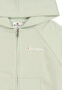 Felpa zip in verde chiaro con una vestibilità comoda, dotata di cappuccio, polsini a coste e un piccolo logo ricamato bianco e rosso sul lato sinistro del petto.