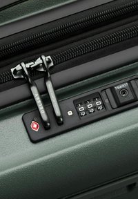 Deux tirettes de fermeture éclair verrouillées dans un cadenas à combinaison approuvé par la TSA sur une valise texturée vert foncé avec des glissières noires.