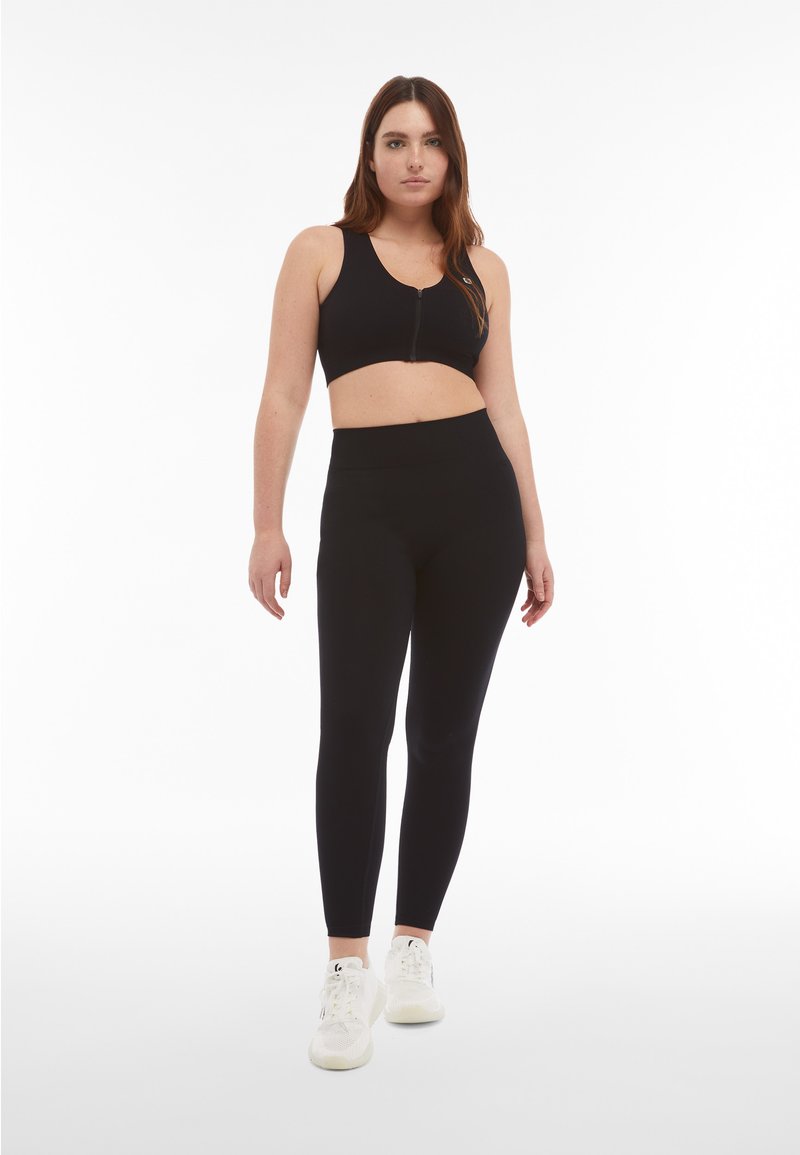 Top sportivo nero con zip frontale, abbinato a leggings neri a vita alta. Entrambi presentano una texture liscia e un design aderente.