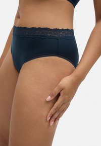 Bañadores hipster de canalé azul marino con un borde de encaje en la cintura, que presentan una textura suave y un diseño clásico.