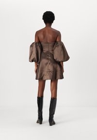 Barna selyem off-shoulder ruha puff ujjakkal, illeszkedő felsőrésszel és harang alakú szoknyával. Térd feletti fekete texturált csizmával párosítva.