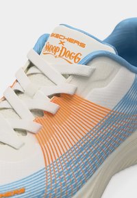 Λευκό αθλητικό παπούτσι με μπλε και πορτοκαλί ριγέ σχεδιασμό, λευκά κορδόνια και τη σήμανση "Skechers x Snoop Dogg" στη γλώσσα.