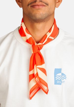 Homme portant une chemise blanche avec un logo bleu et une écharpe à motifs rouges et crème nouée autour du cou.