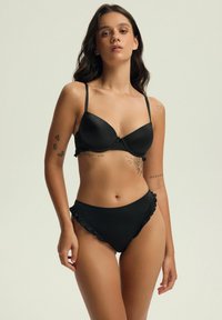 Czarny zestaw bikini z wyściełanym topem na regulowanych ramiączkach i falbankami na wysoko-talii dolnej części. Gładka, matowa tekstura.