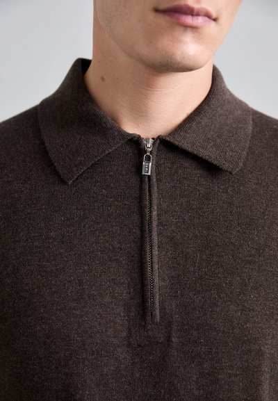 Suéter de color marrón oscuro con cremallera, que presenta un cuello con solapa, textura de punto y un acento de cremallera plateada en la parte frontal.