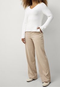 White knit sweater with a V-neck, paired with beige wide-leg trousers. Textured fabric with long sleeves and slight side slits.