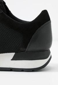 Černé tenisky s síťovaným svrškem, semišovými akcenty a bílou mezipodešví. Design zahrnuje nízkoprofilový siluetu a texturované materiály.