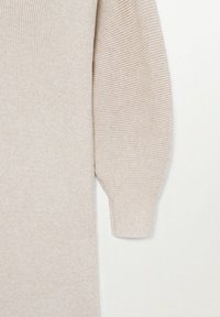 Pull en maille côtelée beige avec des manches bouffantes. Texture douce, design ajusté et silhouette longue. Pas d'ornements ni de motifs visibles.