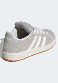 Šedé semišové tenisky s bílými tkaničkami a třemi bílými pruhy; gumová podrážka s hnědým dnem; polstrovaný jazyk a podpora kotníku.