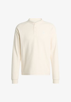 Kremena dugosvjetla pulover majica s vaflastom teksturom, okruglim ovratnikom i plaketom sa tri gumba; na prsima se nalazi mali logo.