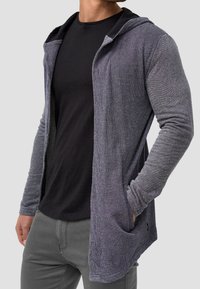 Langer grauer Kapuzen-Cardigan aus strukturiertem Stoff, mit offenem Vorderteil, zwei Fronttaschen und eng anliegenden Ärmeln.