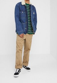 Denimjakke med pelskrave, grøn og hvid stribet skjorte, khaki bukser og sorte Vans sneakers. Casual pasform med flere lommer.