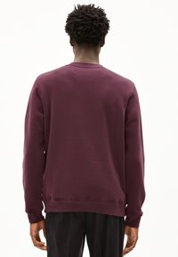 Felpa bordeaux con colletto rotondo, maniche lunghe, polsini a coste e una texture liscia. Design semplice senza loghi o motivi visibili.
