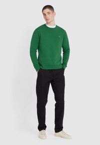 Groene trui met lange mouwen en ronde hals, gecombineerd met zwarte broek en lichte sneakers, gestructureerde stof, eenvoudig logo-detail.