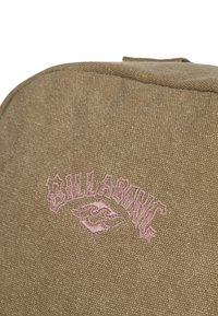 Borsa in tessuto marrone con superficie текстurizzata, forma arrotondata e logo ricamato rosa con lettering stilizzato e design grafico.