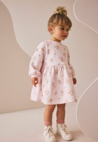 Robe rose avec un motif floral, des manches bouffantes et une jupe évasée. Assortie à des baskets blanches et des chaussettes roses à la cheville.