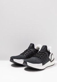 Czarno-białe buty sportowe z teksturowaną siateczką, wyraźnym trzema paskami, grubą amortyzowaną podeszwą i zaokrąglonym czubkiem.