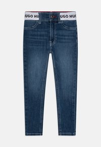 Tmavě modré džíny z denimu s přiléhavým střihem, s bílým páskem s potiskem "HUGO HUGO", designem s pěti kapsami a jemnými švy.