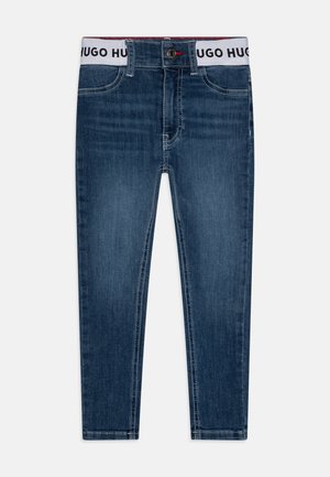 Jeans de ganga azul escuro com um corte ajustado, apresentando uma cintura branca com a impressão "HUGO HUGO", design de cinco bolsos e detalhes de costura subtil.