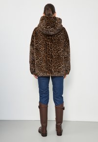 Veste en fausse fourrure à imprimé léopard avec une capuche, motif marron et noir, coupe oversize, associée à un jean bleu et des bottes hautes marron.
