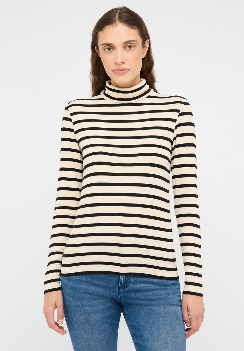 Haut à col roulé rayé crème et noir, avec manches longues et texture côtelée, associé à un jean bleu.