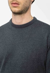 Dunkelgrauer Pullover mit rundem Hals, glatter Textur und geripptem Kragen. Nahaufnahme von Ausschnitt und oberem Brustbereich.