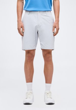 Mand iført lysegrå knælange shorts, hvide sokker og hvide sneakers, der står mod en ensfarvet baggrund.