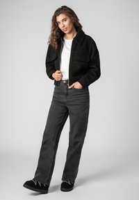 Black fleece cropped jacket with a collar, two front pockets, white t-shirt underneath, paired with high-waisted gray jeans and black shoes.