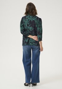 Blouse noire à imprimé floral vert, manches trois-quarts et coupe ample ; associée à un jean en denim bleu à jambes larges et des talons noirs.
