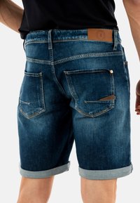 Pantalones cortos de denim en azul oscuro con puños doblados, que cuentan con bolsillos traseros y una etiqueta de cuero marrón en la cintura para la marca.