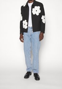 Chaqueta negra con apliques florales blancos, combinada con jeans de mezclilla azul claro y zapatos de cuero negros. Camiseta blanca debajo de la chaqueta.