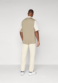 Collared, short-sleeve shirt in tan and white, paired with cream pants; features a straight cut and seam details. Athletic shoes complete the look.