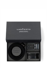 Czarny skórzany pasek umieszczony w czarnym pudełku prezentowym, z dwoma metalowymi klamrami, okrągłym skórzanym uchwytem oraz gładkim, fakturowanym wykończeniem.