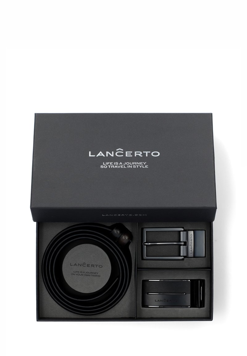 Czarny skórzany pasek umieszczony w czarnym pudełku prezentowym, z dwoma metalowymi klamrami, okrągłym skórzanym uchwytem oraz gładkim, fakturowanym wykończeniem.