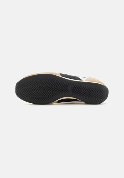 Black sports shoe sole with a herringbone pattern, beige accents, rubber material, and a textured surface for traction.