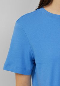 Sininen puuvillapaita, jossa on lyhyet hihat, pyöreä kaula-aukko ja hienovaraiset ompeluyksityiskohdat, tarjoten sileän tekstuurin ja rennon istuvuuden.