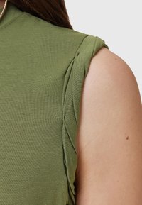 Olivgrön ärmlös topp med en j�ämn textur och rynkad detalj på axeln, samt en diskret rundad halsringning.