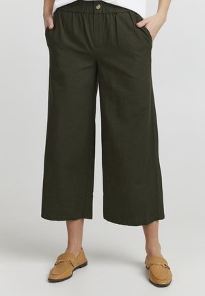 Culottes en lin vert foncé avec une taille élastique, des poches latérales et une coupe décontractée, accompagnés de chaussures à enfiler marron clair.
