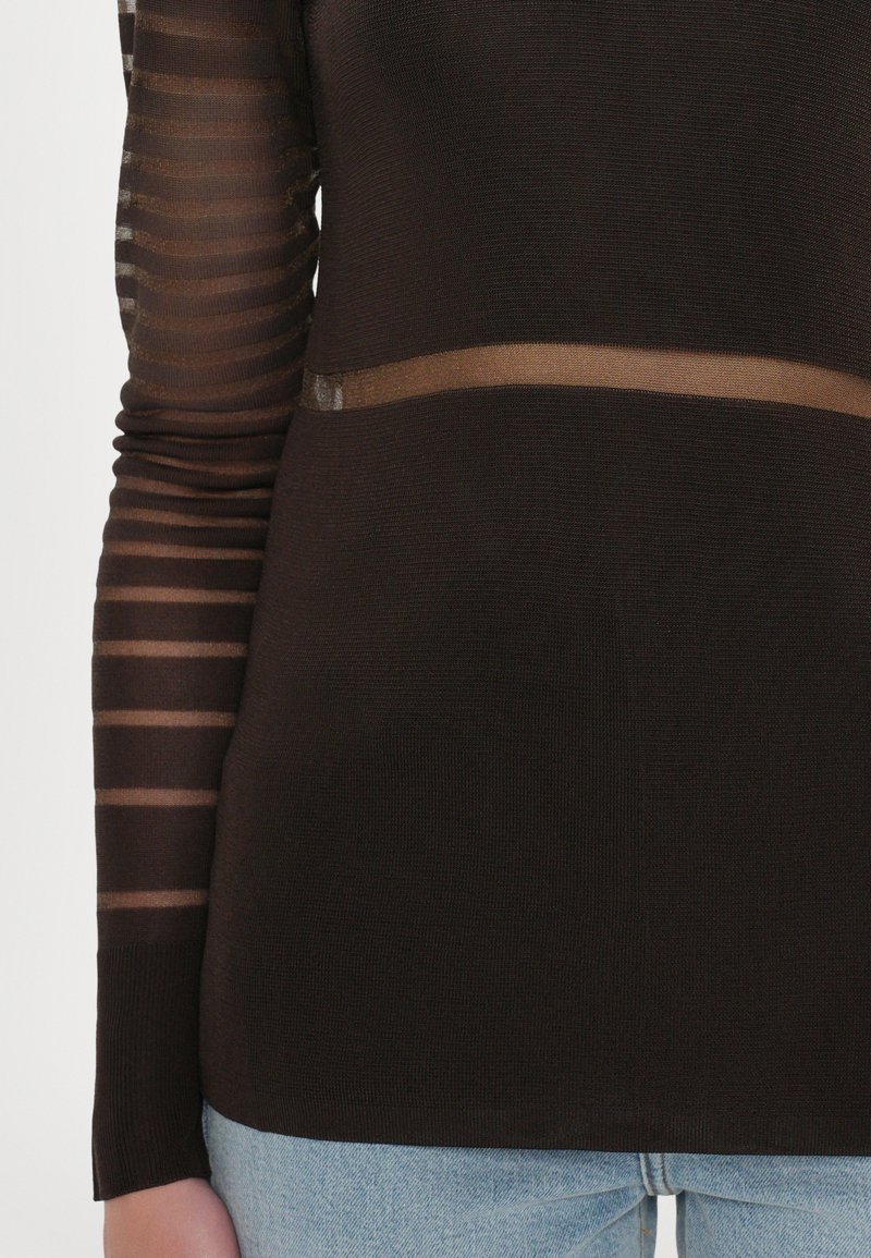 Top nero a maniche lunghe con maniche a strisce trasparenti, caratterizzato da una banda orizzontale trasparente in vita, realizzato in un tessuto testurizzato.