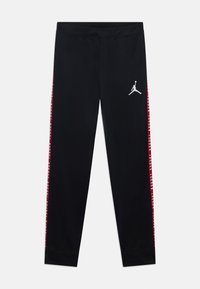 Pantalons de sport noirs à coupe slim, avec des bandes latérales rouges et un logo Jumpman blanc sur la cuisse supérieure gauche. Texture de tissu lisse.