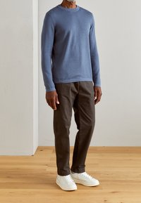 Maglione a maniche lunghe di un blu chiaro con scollatura rotonda abbinato a pantaloni dritti marroni scuri e sneakers bianche con accenti delicati.