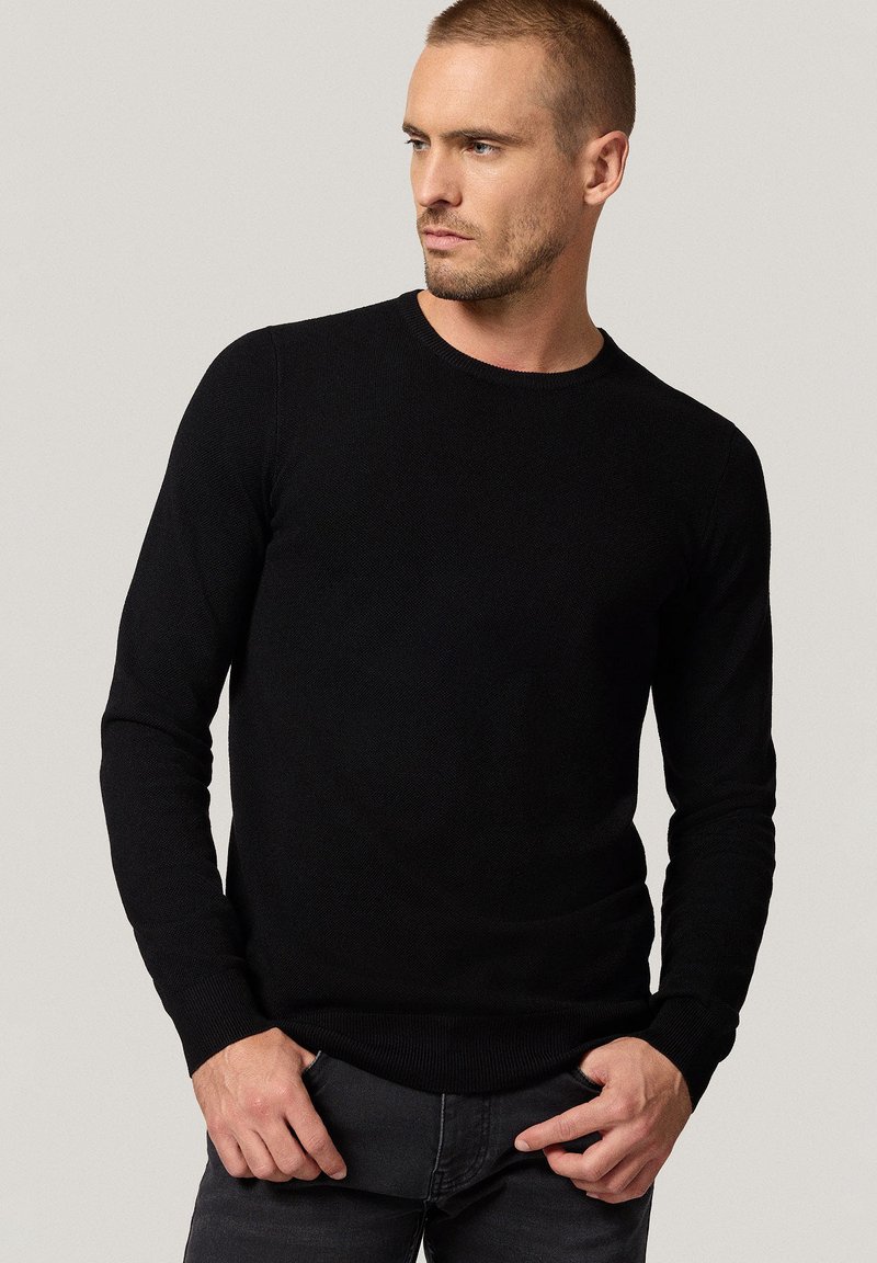 Czarny sweter z długim rękawem wykonany z dzianiny, z okrągłym dekoltem, prążkowanymi mankietami i dolnym wykończeniem, o dopasowanym kroju i gładkiej fakturze.