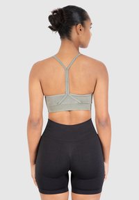 Kirkas vihreä urheil bra, jossa on ohuet hihnat ja kohopintainen rakenne, yhdistettynä korkeavyötäröisiin mustiin shortseihin, joissa on sileä pinta ja hillitty kuvio.