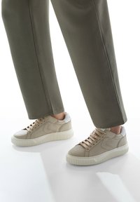 Sneaker in pelle beige con tomaia texturizzata, suola in gomma crema e dettagli metallici argento sul tallone; allacciate con lacci beige chiaro.