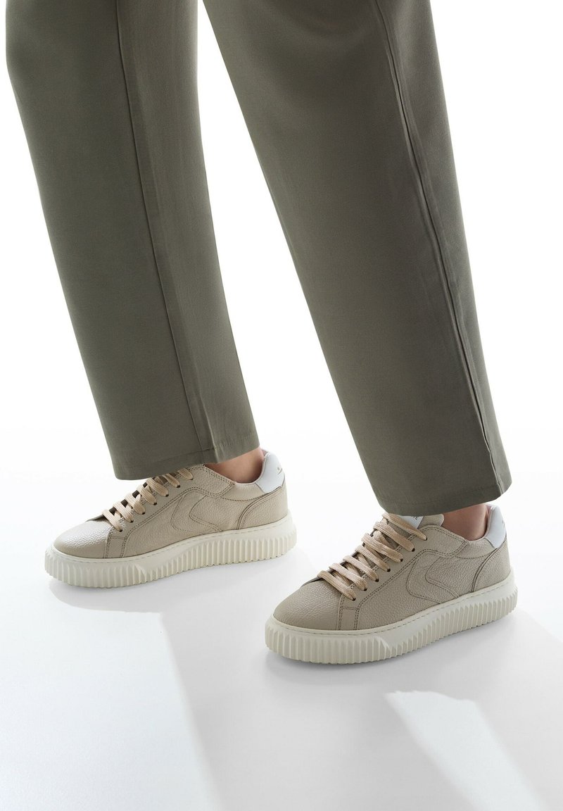 Sneaker in pelle beige con tomaia texturizzata, suola in gomma crema e dettagli metallici argento sul tallone; allacciate con lacci beige chiaro.