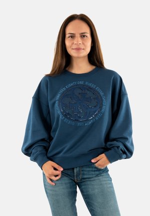 Blauwe oversized sweatshirt met een circulair logo met tekst in een contrasterende donkere tint; gemaakt van zacht, textuurmateriaal.