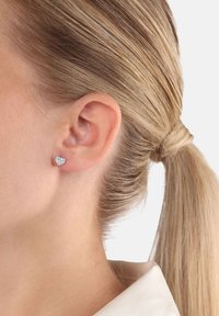 Orecchino a perno a forma di cuore in argento sterling con superficie texturizzata, caratterizzato da pietre preziose trasparenti incastonate in una cornice lucida.